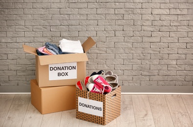 Photo of Donation boxes with clothes and shoes on floor against brick wall