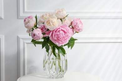 Photo of Beautiful peonies in glass vase on white table. Space for text