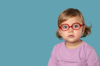 Photo of Cute little girl in glasses on light blue background. Space for text