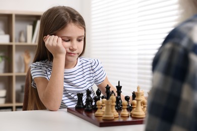 Photo of Girl playing chess with her grandfather at table in room