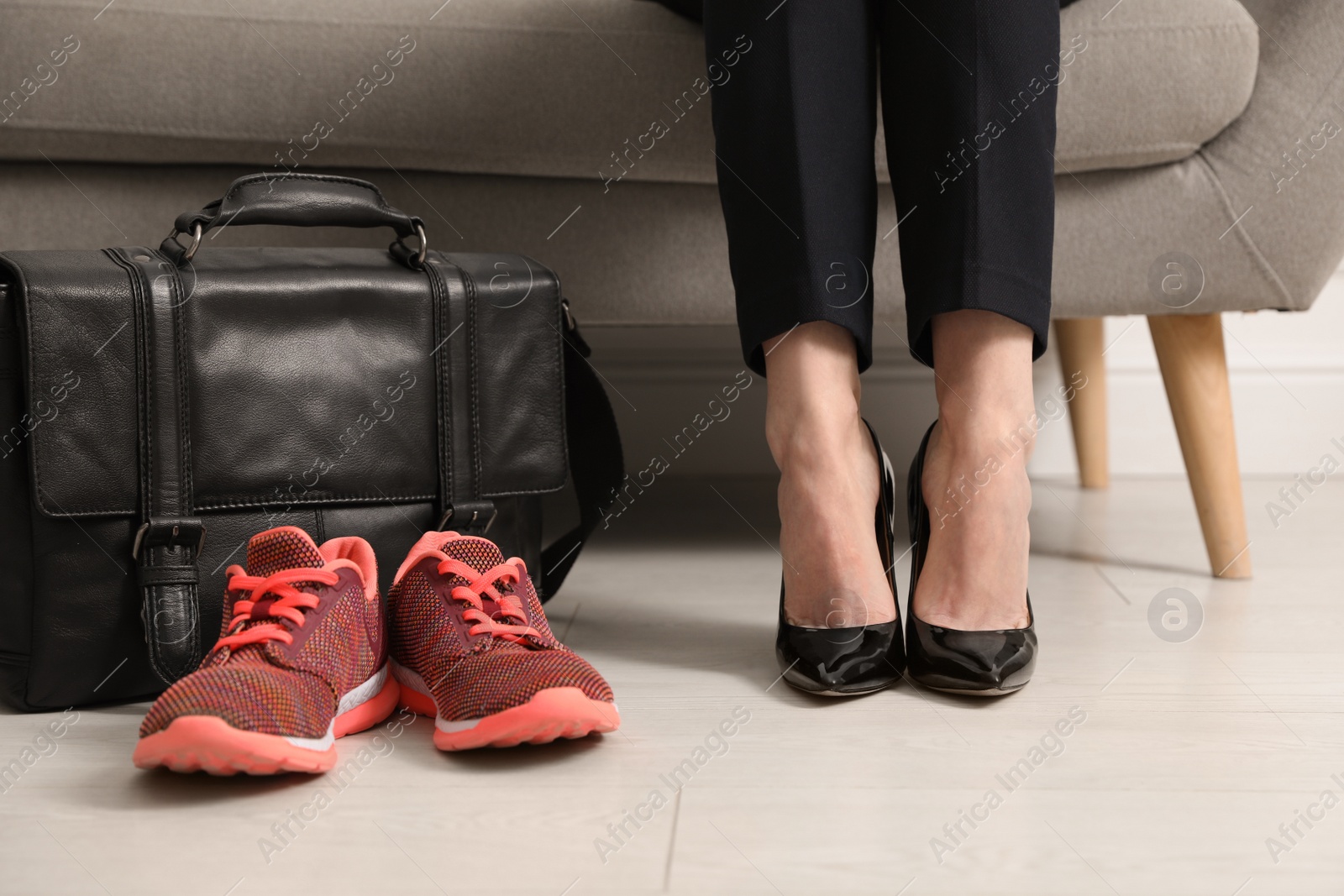 Photo of Woman in high heel shoes sitting on sofa near comfortable sneakers in office, closeup