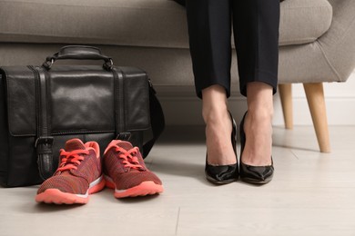 Photo of Woman in high heel shoes sitting on sofa near comfortable sneakers in office, closeup