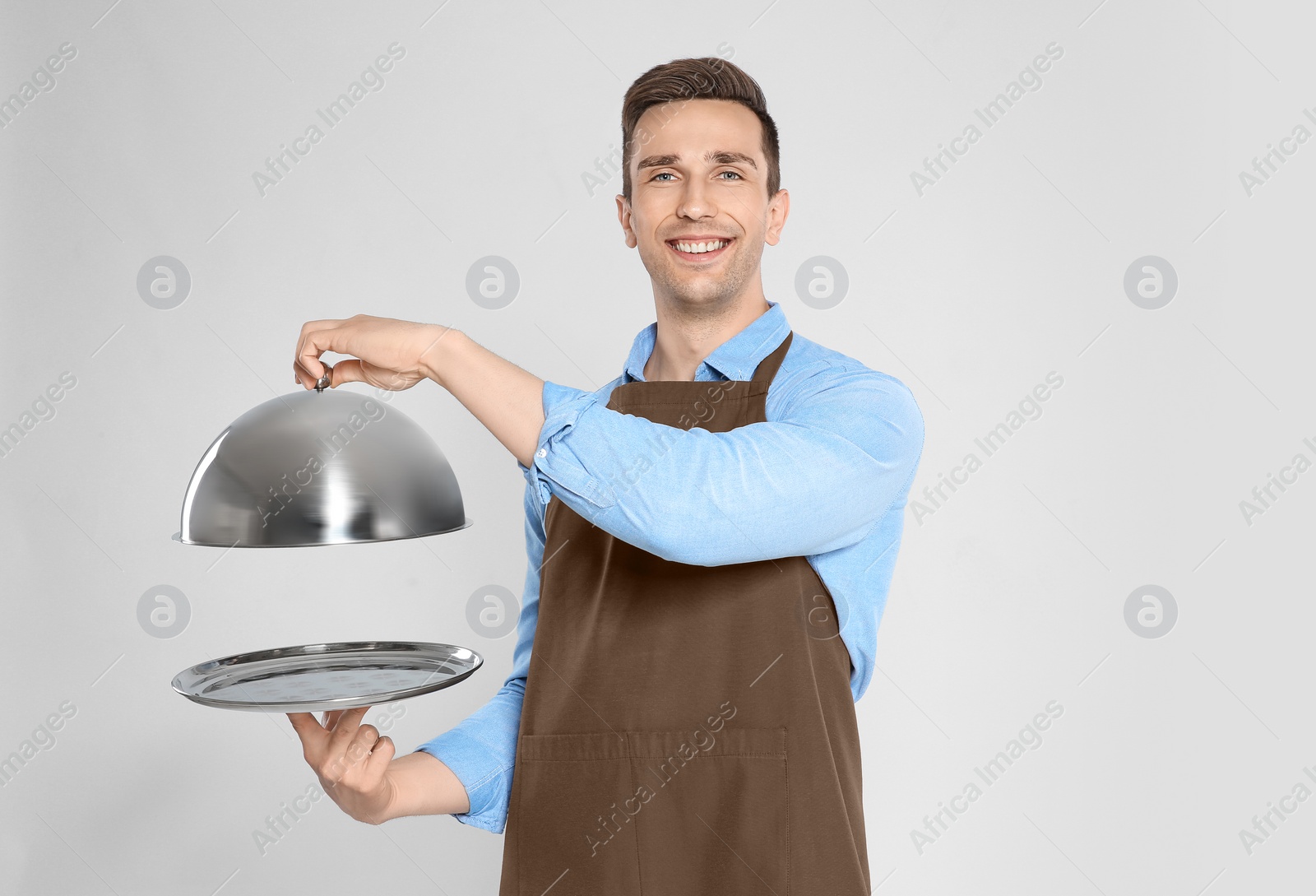 Photo of Handsome waiter holding metal tray with lid on light background