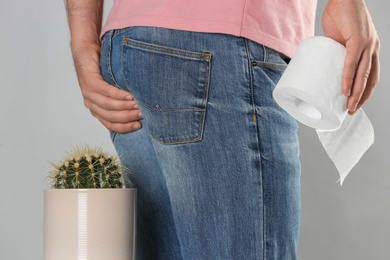 Man with toilet paper sitting down on cactus against light grey background, closeup. Hemorrhoid concept