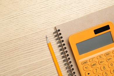 Calculator, notebook and pencil on wooden table, top view with space for text. Tax accounting
