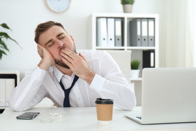 Photo of Lazy young man yawning at table in office