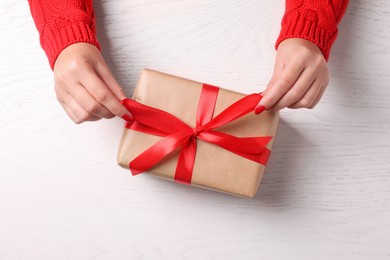 Photo of Christmas present. Woman with gift box at white wooden table, top view