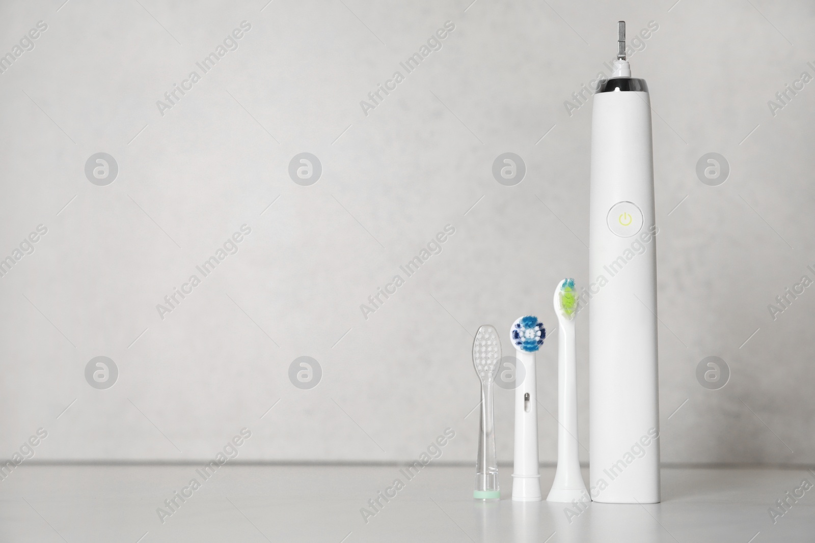 Photo of Electric toothbrush and replacement brush heads on light background, space for text