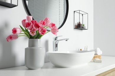 Vase with beautiful pink tulips near sink in bathroom