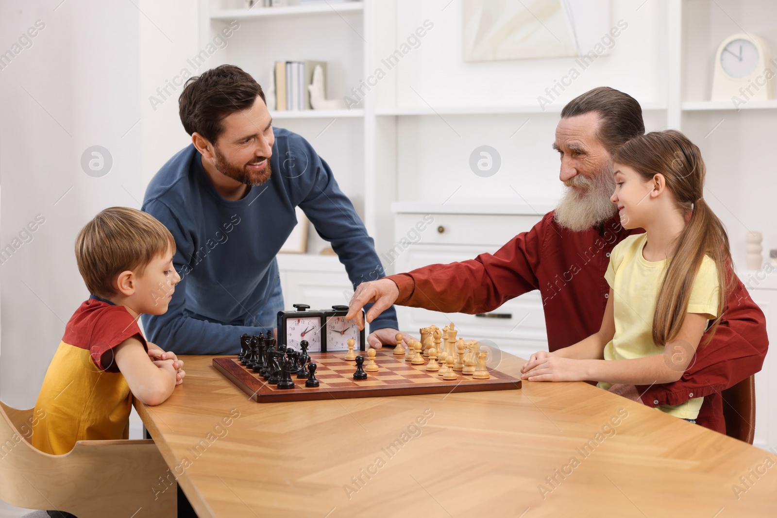 Photo of Family playing chess together at table in room