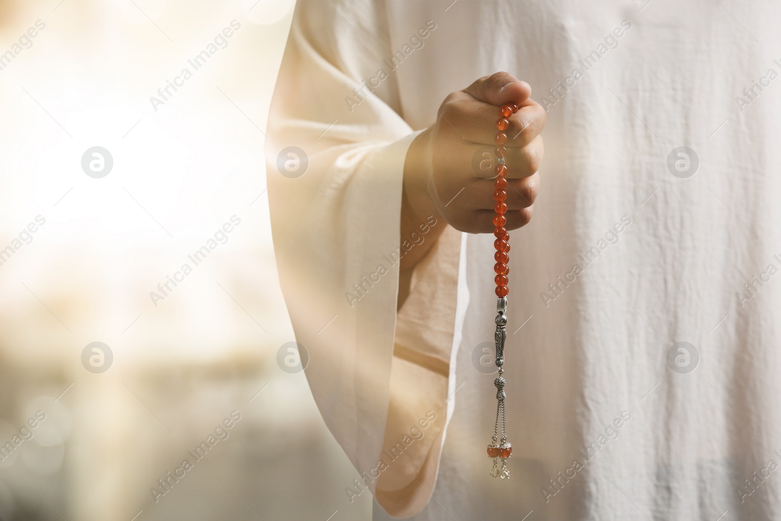 Image of Muslim man with misbaha praying on blurred background, closeup. Space for text