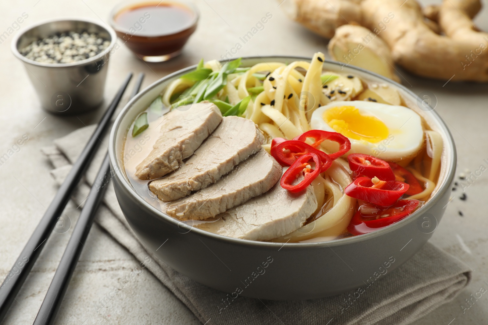 Photo of Delicious ramen in bowl and chopsticks on light textured table, closeup. Noodle soup