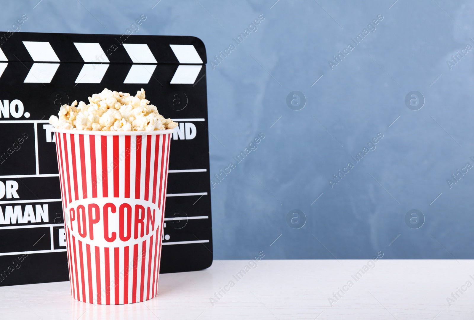 Photo of Delicious popcorn and clapper on white wooden table. Space for text