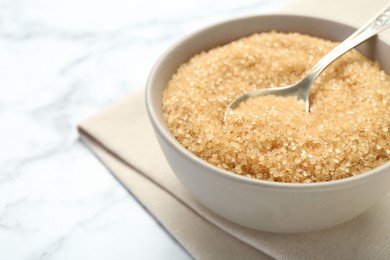 Photo of Brown sugar in bowl and spoon on white marble table, closeup. Space for text