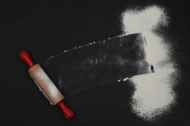 Photo of Flour and rolling pin on black table, top view. Space for text