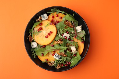 Photo of Tasty salad with persimmon, blue cheese, pomegranate and walnuts on orange background, top view