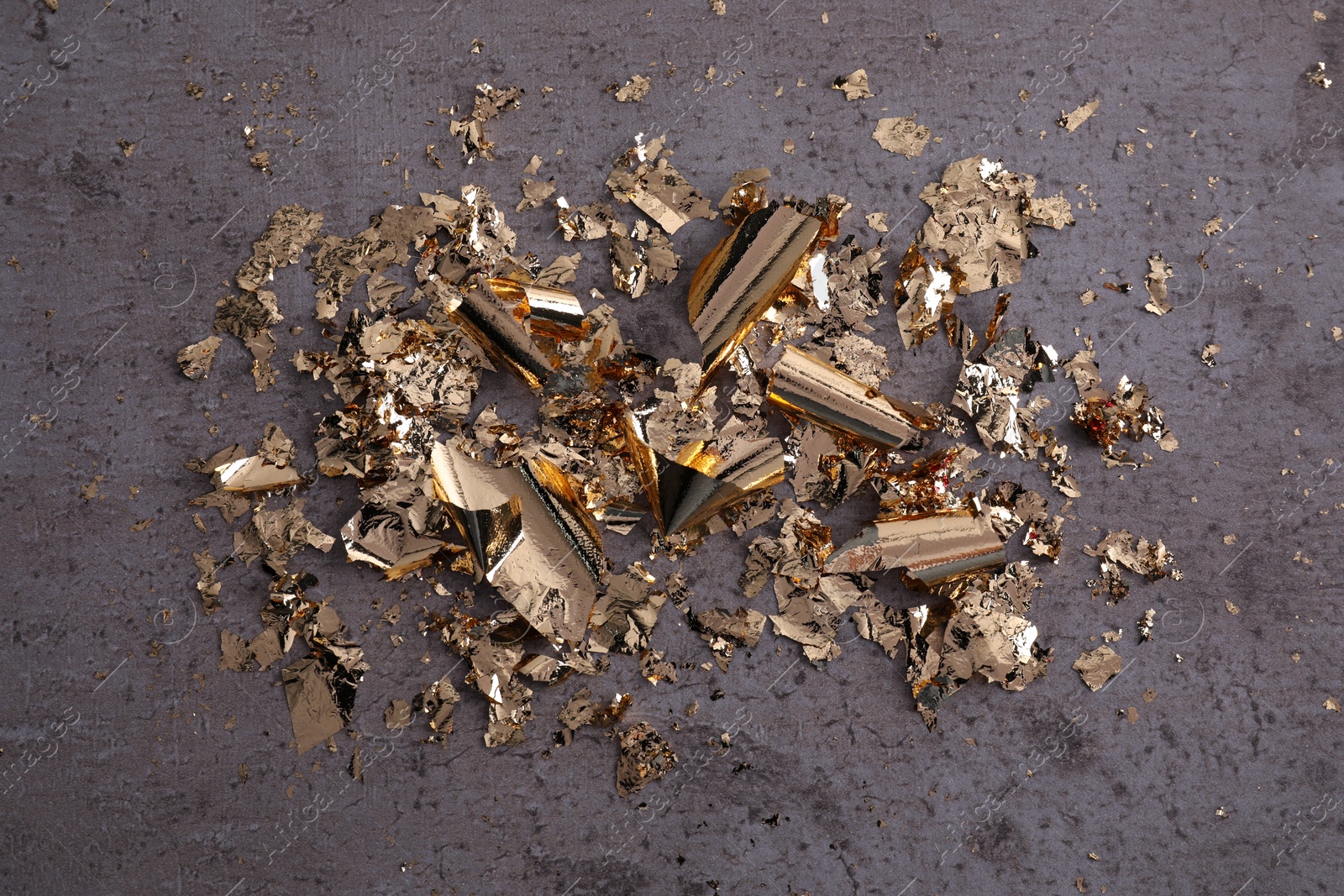 Photo of Many pieces of edible gold leaf on grey textured table, flat lay