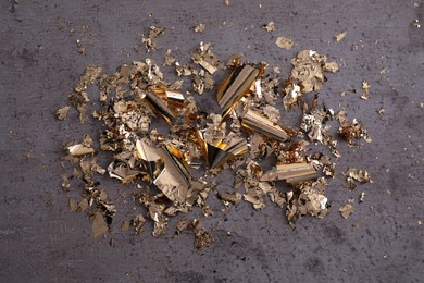 Many pieces of edible gold leaf on grey textured table, flat lay