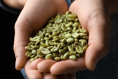 Photo of Woman holding pile of green coffee beans on black background, closeup