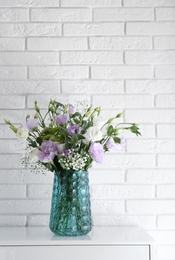Photo of Bouquet of beautiful Eustoma flowers on cabinet near white brick wall