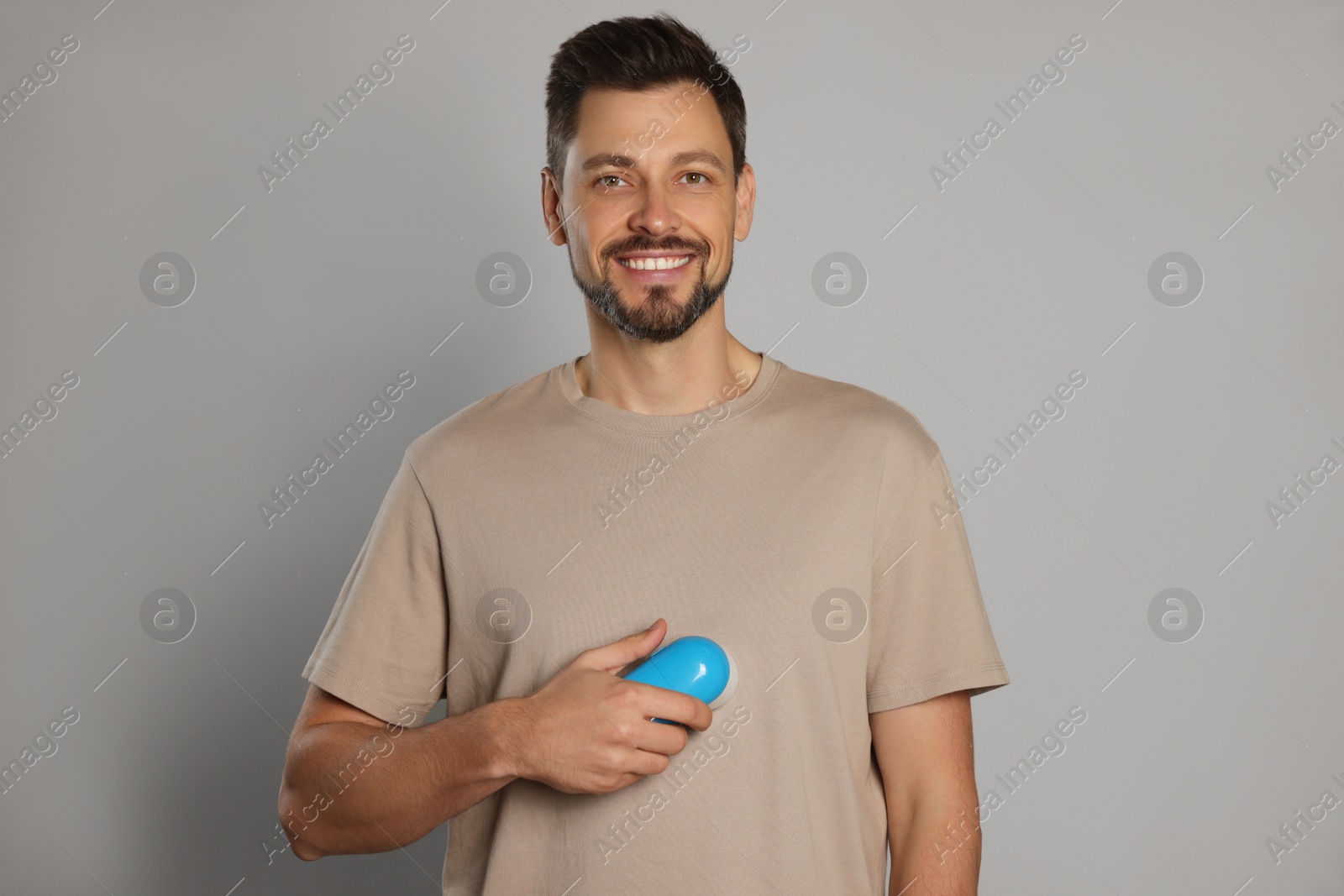 Photo of Handsome man using fabric shaver on light grey background