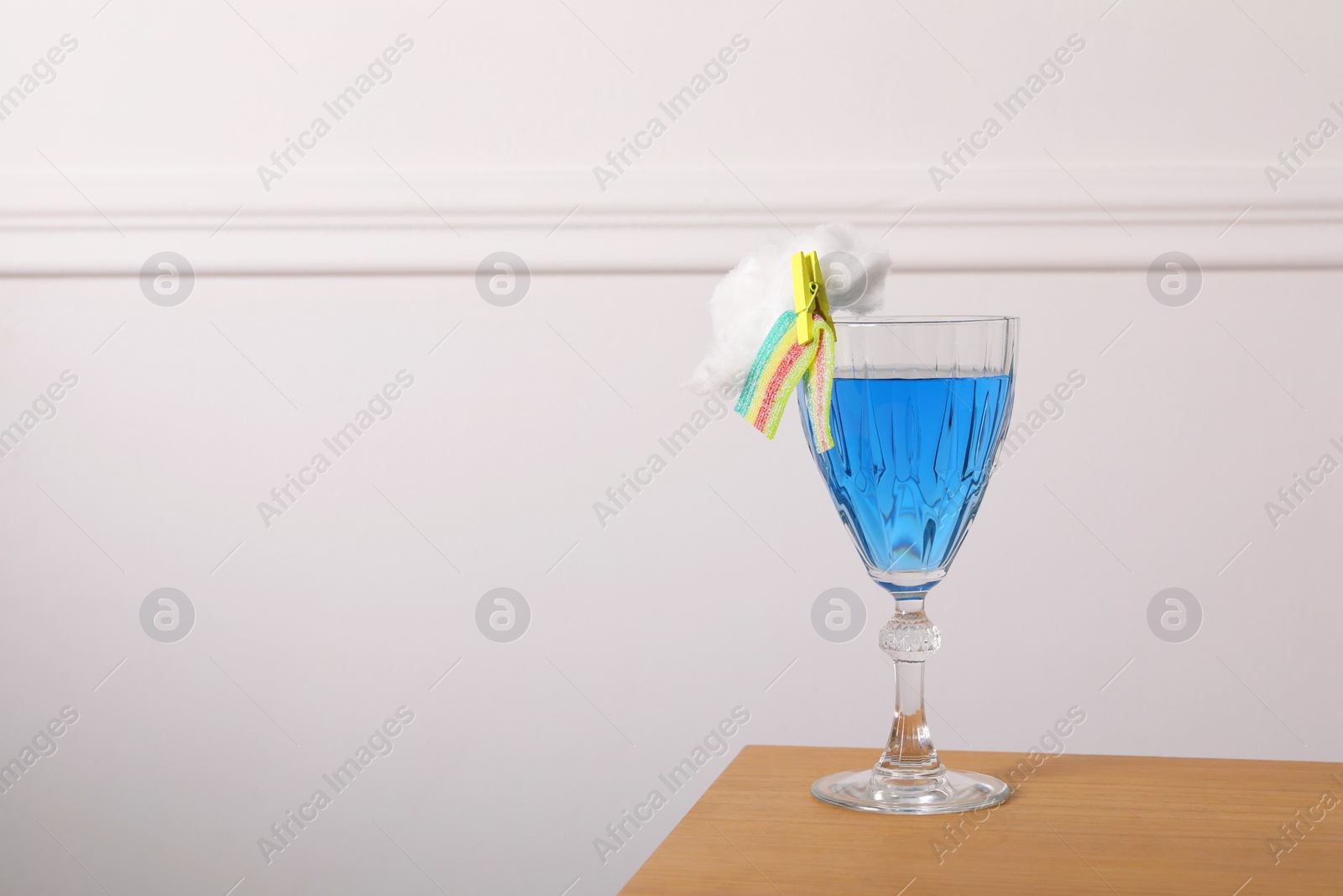 Photo of Bright cocktail in glass decorated with cotton candy and sour rainbow belt on wooden table, space for text