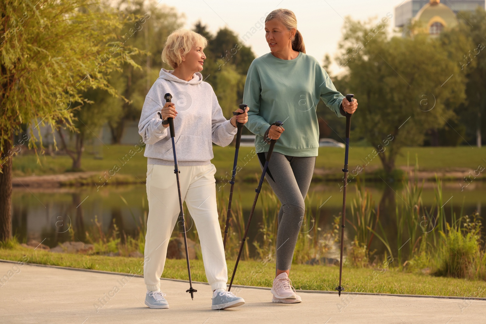 Photo of Two senior friends performing Nordic walking outdoors