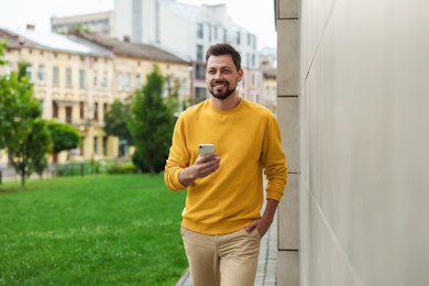 Handsome man with smartphone walking on city street