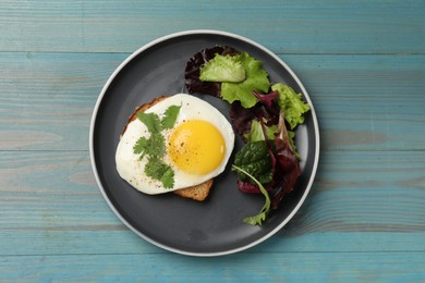 Photo of Plate with tasty fried egg, slice of bread and salad on light blue wooden table, top view