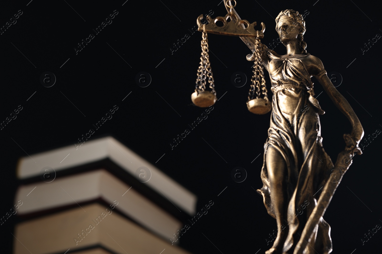Photo of Symbol of fair treatment under law. Statue of Lady Justice near books on dark background, low angle view with space for text