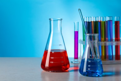 Different laboratory glassware with colorful liquids on wooden table against light blue background. Space for text