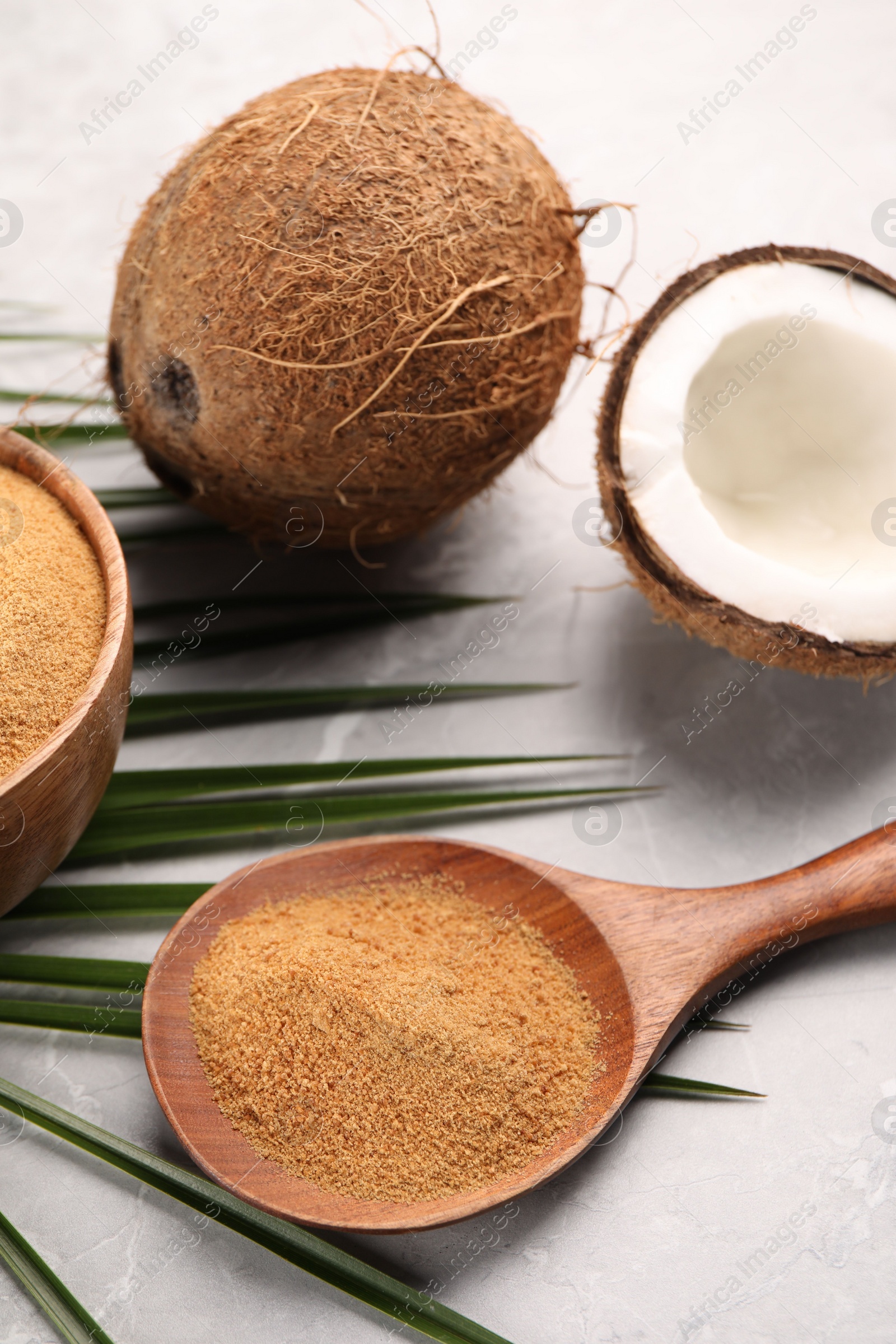 Photo of Spoon with coconut sugar, palm leaves and fruit on light marble table, closeup