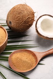 Photo of Spoon with coconut sugar, palm leaves and fruit on light marble table, closeup