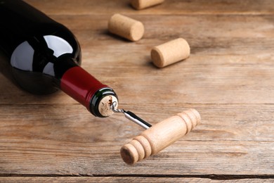 Photo of Opening wine bottle with corkscrew on wooden table, closeup. Space for text