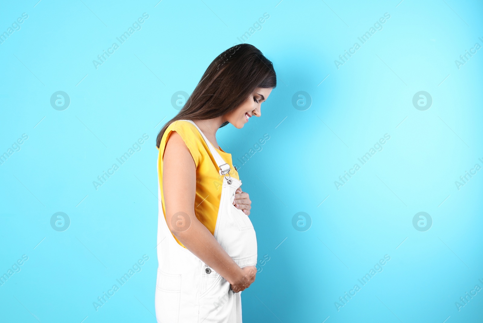 Photo of Happy pregnant woman posing on color background. Space for text