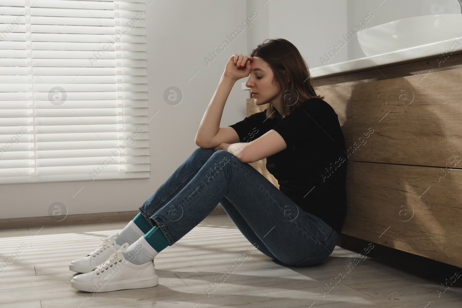 Photo of Sad young woman sitting on floor indoors