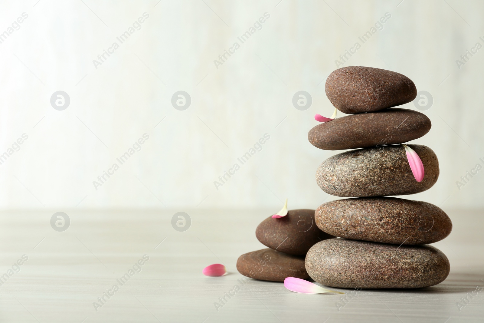 Photo of Stack of spa stones and petals on table against white background, space for text