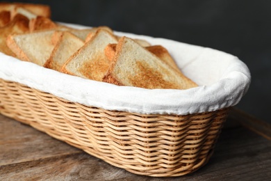 Slices of toasted bread in basket on wooden table, closeup