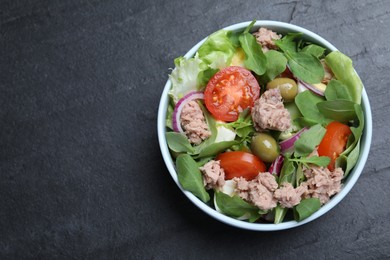 Photo of Bowl of delicious salad with canned tuna and vegetables on black table, top view. Space for text