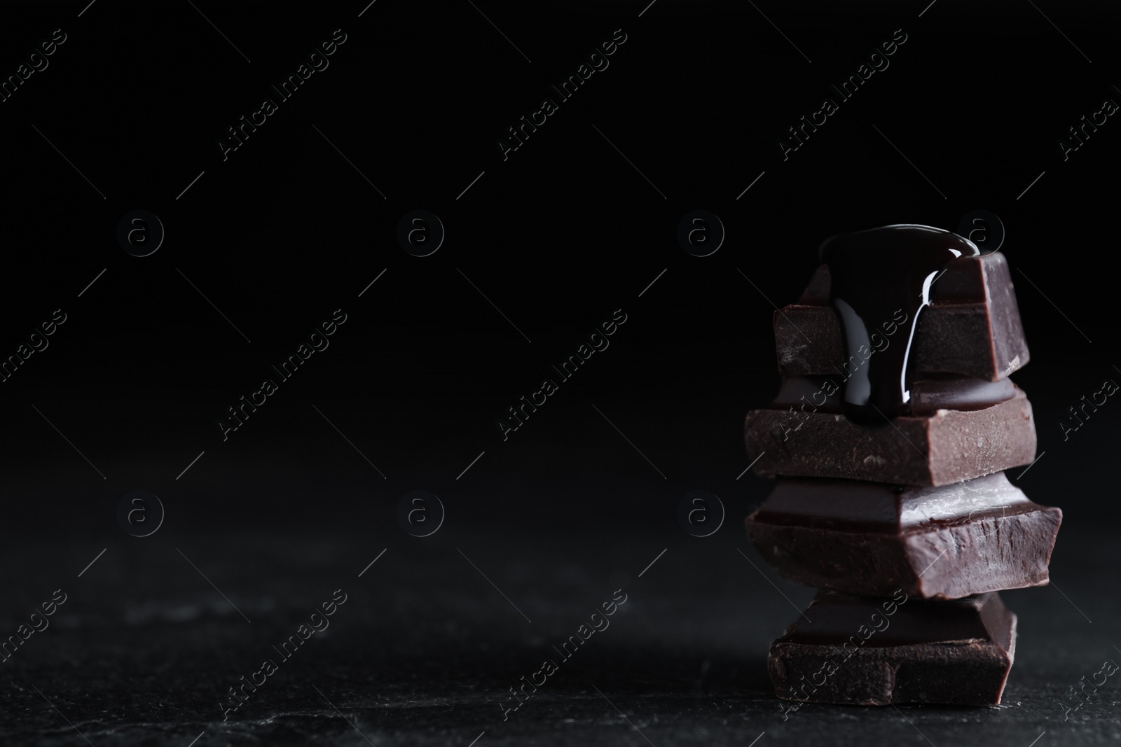 Photo of Delicious dark chocolate with syrup on black table. Space for text