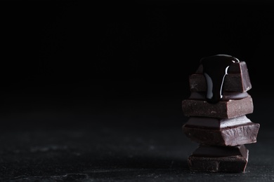 Photo of Delicious dark chocolate with syrup on black table. Space for text