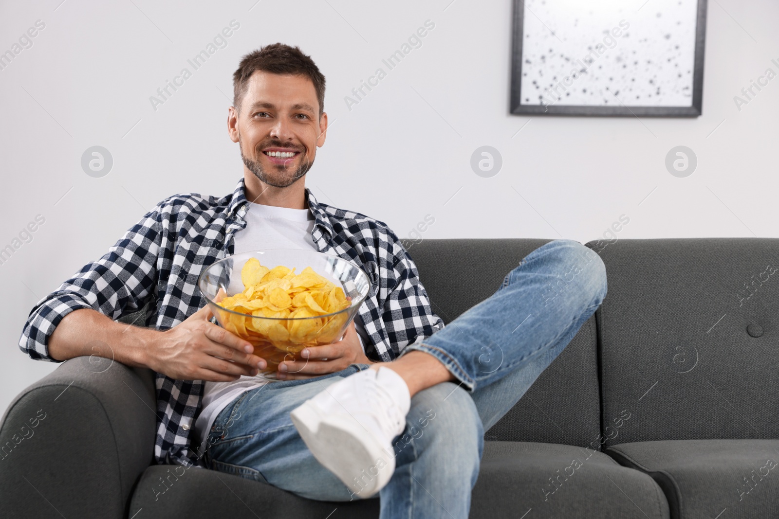 Photo of Handsome man eating potato chips on sofa at home