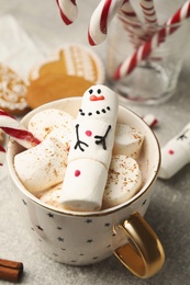 Photo of Funny marshmallow snowman in cup of hot drink on light grey table, above view