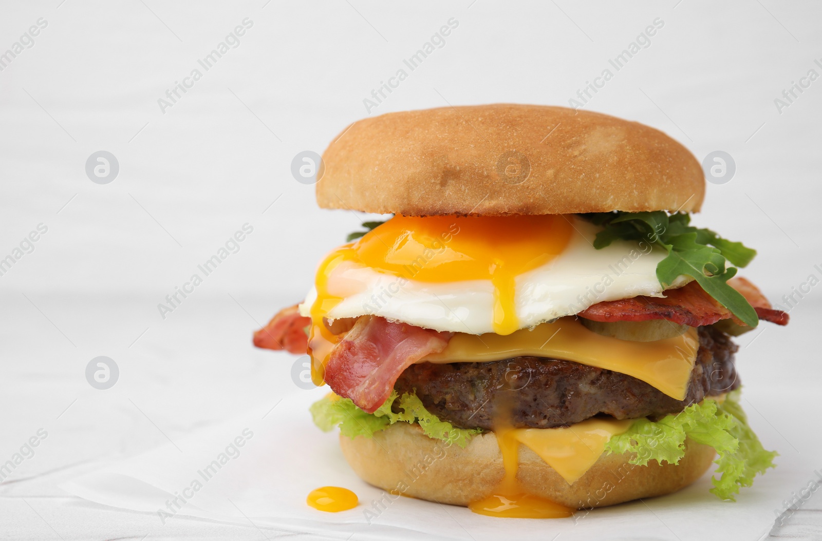 Photo of Delicious burger with fried egg on white table, closeup. Space for text