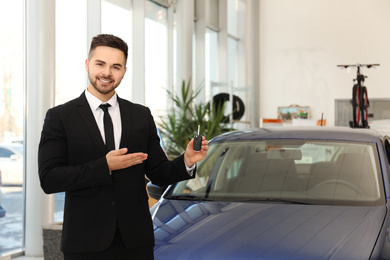 Young salesman with key near car in dealership