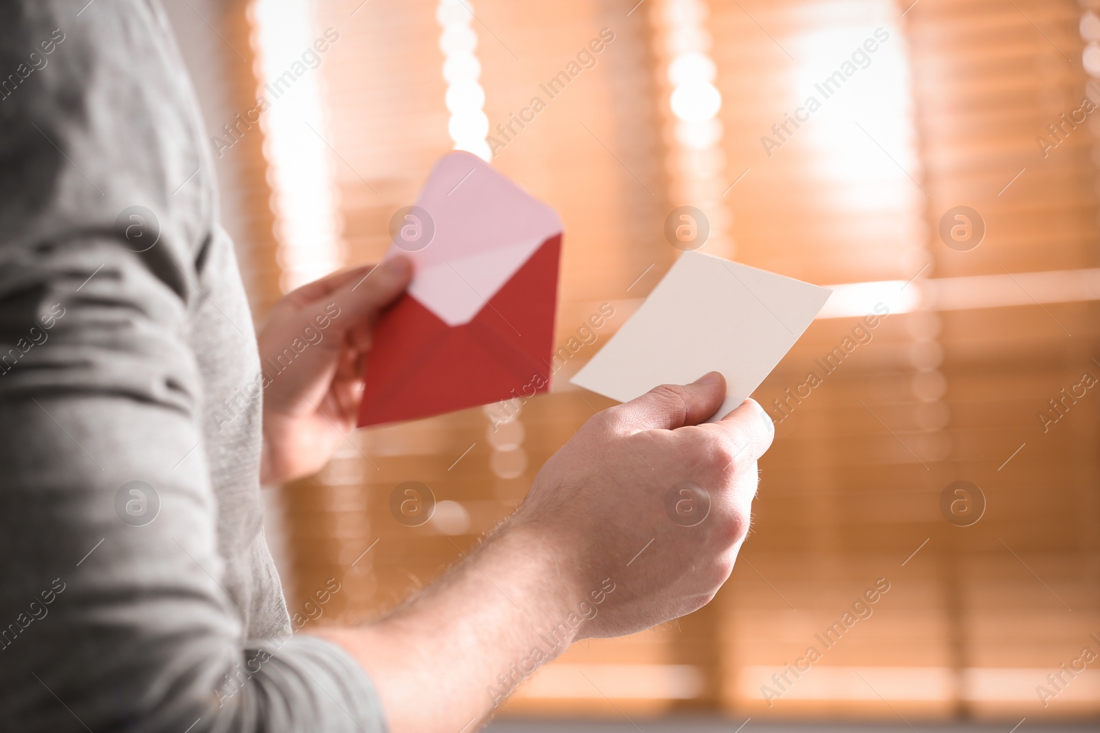 Photo of Man holding envelope with blank greeting card indoors. closeup