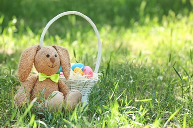 Photo of Toy bunny and basket with Easter eggs on grass