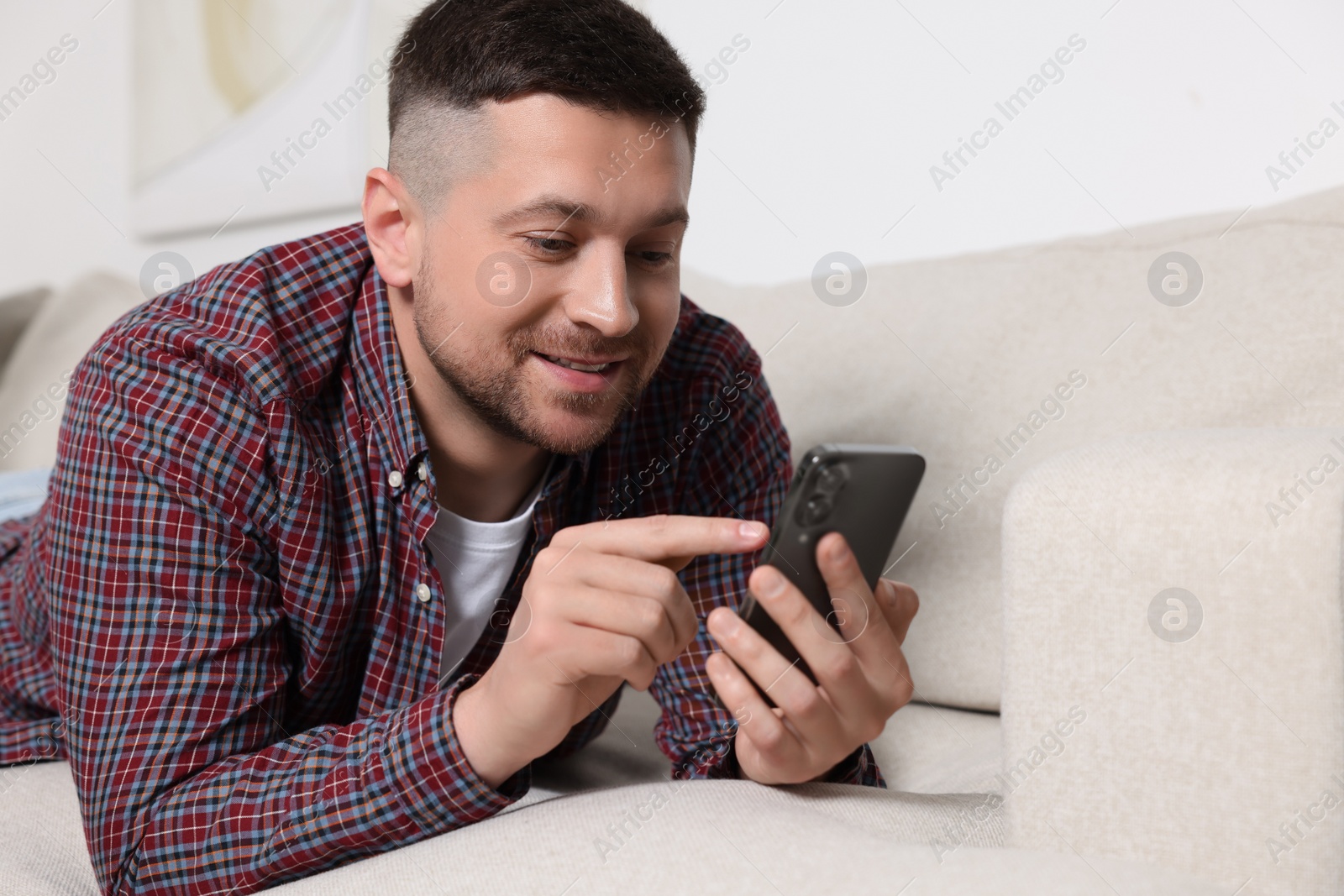 Photo of Handsome man sending message via smartphone on sofa at home