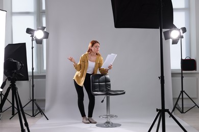 Photo of Casting call. Emotional woman with script performing on grey background in modern studio