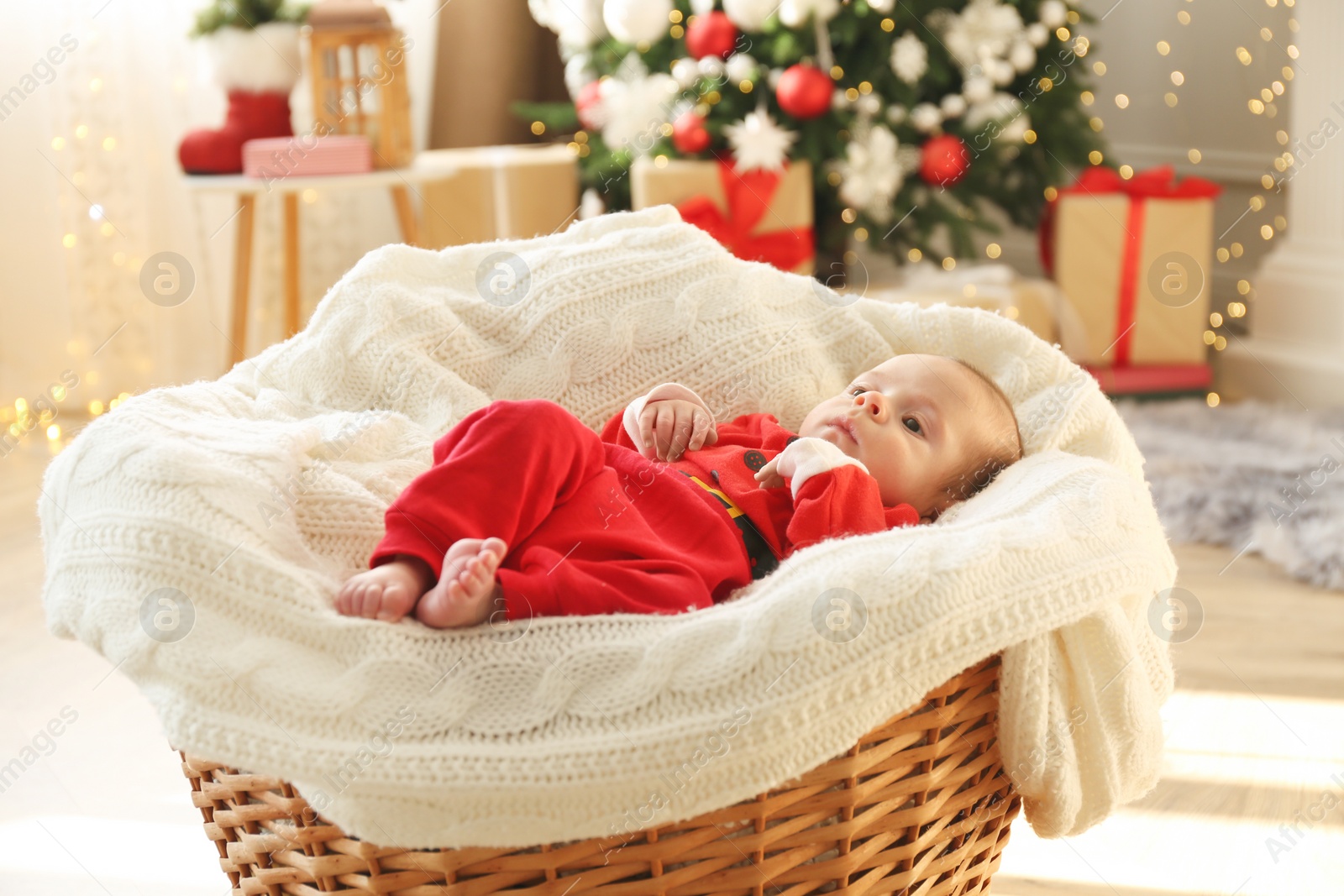 Photo of Cute little baby on knitted blanket in room decorated for Christmas